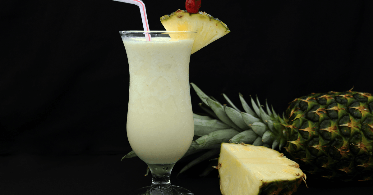 Ein Glas Ananas-Smoothie mit Trinkhalm und Ananasscheibe auf schwarzem Hintergrund.